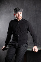 Serious handsome young bearded man in hat on grey background looking at camera. Portrait of man against grey wall.