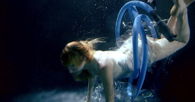 a girl with long hair is drowning in dark water. a plastic wrap and a large blue plastic tube were wrapped around the woman's body. she picks up a disposable plate