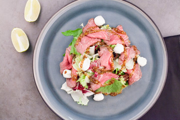 Salad with meat, with greens, on a blue plate, decorated with Cutlery and lemon. Conceptual recipes for salads, meat dishes or restaurant menus.