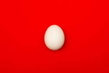 Big ostrich egg isolated on a red background, close up. Organic fresh egg. Concept of healthy food. Ostrich egg as symbol of birth. Huge white egg shell of an african ostrich. Easter concept.