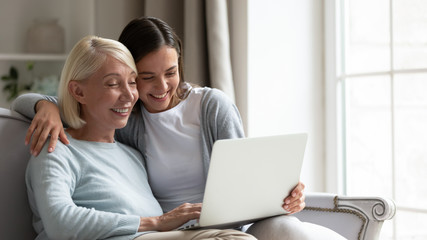 Happy senior mother and adult daughter using laptop together