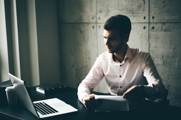 Business man working at office with laptop and documents on his desk. Man wearing white shirt and making notes on the documents.