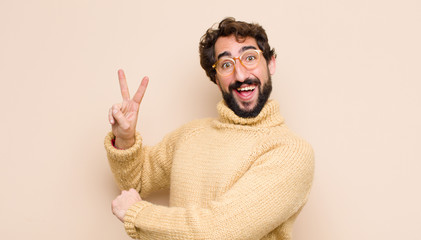 young cool man smiling and looking happy, carefree and positive, gesturing victory or peace with...