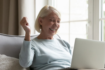 Overjoyed senior woman triumph reading good news on laptop
