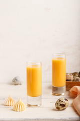 Sweet egg liqueur in glass with quail eggs and meringues on white wooden background. Side view, copy space, vertical.