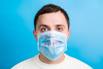 Portrait of young man wearing medical mask with China quarantine word at blue background. Coronavirus concept. Respiratory protection