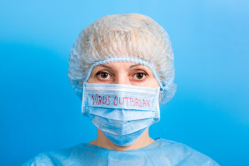 Portrait of woman in medical uniform and mask with virus outbreak word at blue background. Respiratory protection. Coronavirus concept