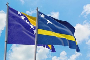 Curacao and Bosnia Herzegovina flags waving in the wind against white cloudy blue sky together....
