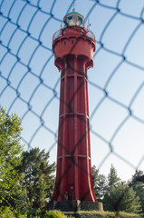 A red lighthouse behind a fence on a clear sky