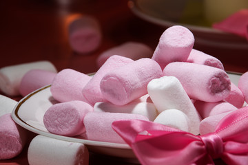 White and pink marshmallows on a saucer and sprinkled on a pink background.