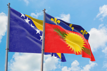 Guadeloupe and Bosnia Herzegovina flags waving in the wind against white cloudy blue sky together. Diplomacy concept, international relations.