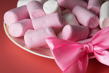 White and pink marshmallows in a saucer on a pink background with a bow.