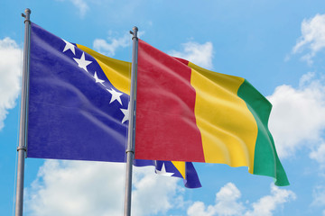 Guinea and Bosnia Herzegovina flags waving in the wind against white cloudy blue sky together. Diplomacy concept, international relations.