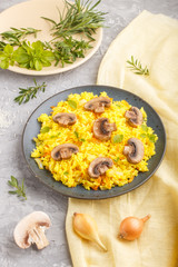 Yellow fried rice with champignons mushrooms, turmeric and oregano on blue ceramic plate on a gray concrete background. side view.