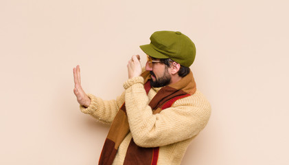 young cool bearded man covering face with hand and putting other hand up front to stop camera,...