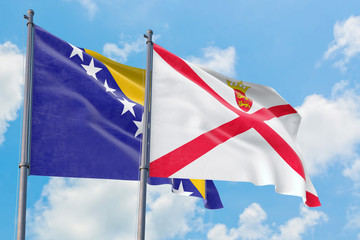 Jersey and Bosnia Herzegovina flags waving in the wind against white cloudy blue sky together. Diplomacy concept, international relations.