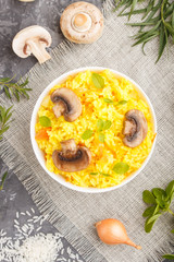 Yellow fried rice with champignons mushrooms, turmeric and oregano in white ceramic bowl on a black concrete background. top view.
