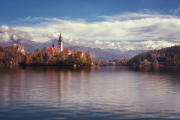 Famous alpine Bled lake (Blejsko jezero) in Slovenia, amazing autumn landscape. Scenic view of the lake, island with church, Bled castle, mountains and blue sky with clouds, outdoor travel background