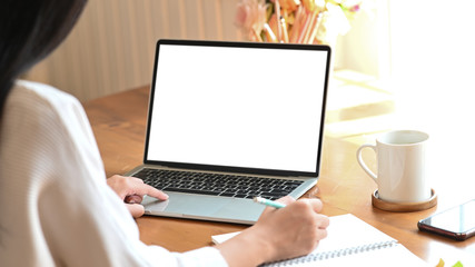 Cropped shot woman using mockup laptop and writing on her diary.