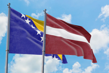 Latvia and Bosnia Herzegovina flags waving in the wind against white cloudy blue sky together. Diplomacy concept, international relations.