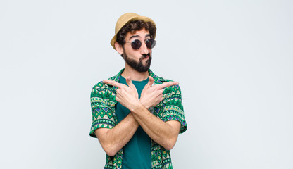 young tourist man looking puzzled and confused, insecure and pointing in opposite directions with...