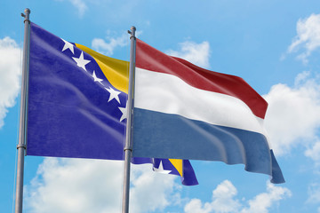 Netherlands and Bosnia Herzegovina flags waving in the wind against white cloudy blue sky together. Diplomacy concept, international relations.