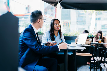 Adult multiracial coworkers having interesting conversation while using digital devices on cafe terrace