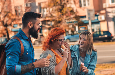 Fototapeta premium Group of tourists enjoying on vacation, young friends having fun walking on city street eating ice cream during sunset.