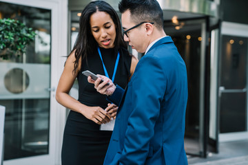 Serious Asian entrepreneur showing mobile to coworker