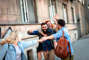 Group of smiling tourists enjoying on vacation, young friends having fun walking on city street during the day.