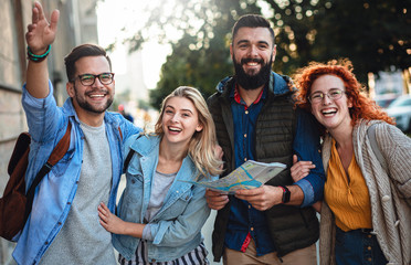 Group of smiling tourists enjoying on vacation, young friends having fun walking on city street...