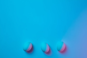 Egg hunt is coming. Easter traditions, pink-blue colored eggs on blue background, neon light top view, copyspace for ad. Concept of holidays, spring, celebrating, food and sweets, family time.