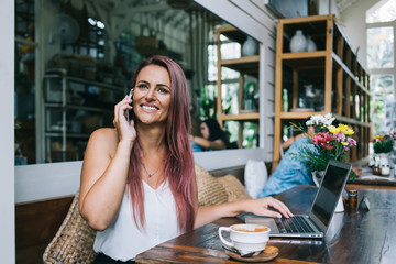Woman having smartphone conversation and browsing laptop in restaurant