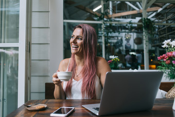 Laughing woman having coffee break while working on laptop
