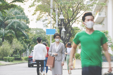 Young Asian businesswoman walking in downtown of her city with medical mask on her face during coronavirus epidemic in country