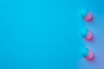 Egg hunt is coming. Easter traditions, pink-blue colored eggs on blue background, neon light top view, copyspace for ad. Concept of holidays, spring, celebrating, food and sweets, family time.