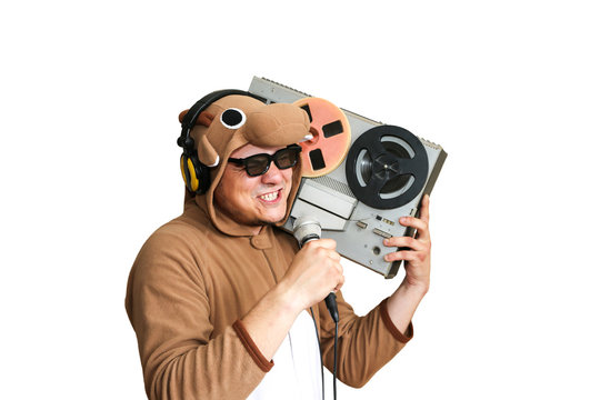 Man in cosplay costume of a cow singing karaoke. Guy in animal pyjamas sleepwear with microphone. Funny photo with reel tape recorder. Party ideas. Disco retro music. Isolated on white background.