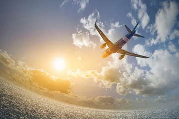 Commercial passenger plane flies over the sea towards the bright summer sun