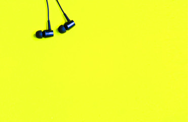 Black earphones lying on the yellow background. Modern music concept. Audio technology.