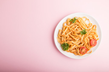 Semolina pasta with tomato pesto sauce, orange and herbs on a pink pastel background. Top view,...
