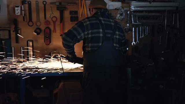 Worker using circular ginder at the workplace. A lot of sparks from metal repair part. View from back. Gimbal shot. Slowmotion.