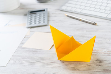 Top view office workspace with orange paper ship