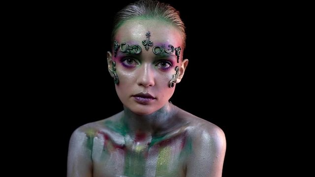 Girl in creative makeup on a black background looks into the camera and moves