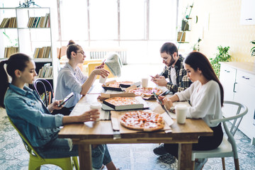 Fellows speaking and surfing smartphones at table with pizza in canteen