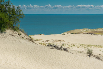 Landscape of sandy beach with sand dunes, sea, and cloudy sky