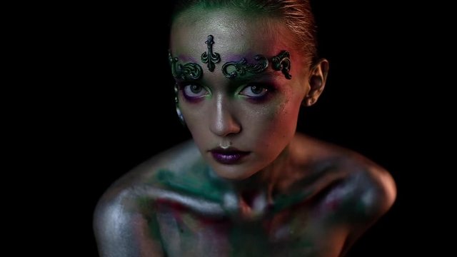 Girl in creative makeup on a black background looks into the camera and moves