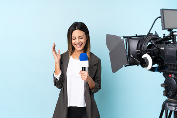 Reporter woman holding a microphone and reporting news over isolated blue background laughing