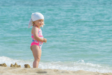 Cute little girl standing in sandy beach on blue sea background
