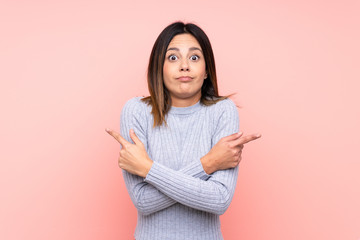 Fototapeta premium Woman over isolated pink background pointing to the laterals having doubts