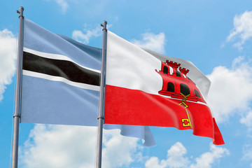 Gibraltar and Botswana flags waving in the wind against white cloudy blue sky together. Diplomacy concept, international relations.